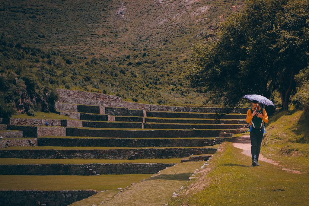 Traveler walking along a scenic pathway beside ancient Inca agricultural terraces in the Peruvian Andes.