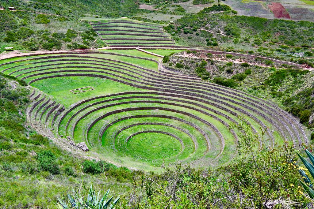 Lush green circular Inca agricultural terraces at Moray in Peru's Sacred Valley, surrounded by vibrant vegetation and rolling Andean hillsides.