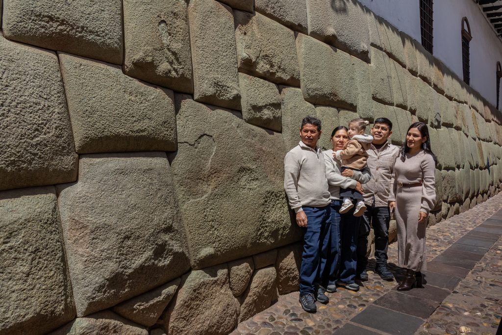 Visitors standing beside a massive ancient Inca stone wall with precisely fitted stone blocks along a cobblestone street in Cusco, Peru.
