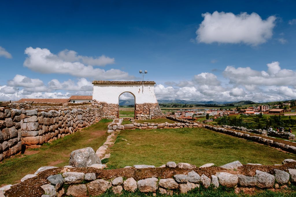Historic stone ruins and white colonial gateway in Chinchero, Peru, overlooking the Sacred Valley beneath a blue Andean sky.