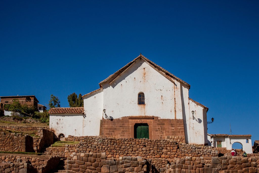 Historic colonial church in Chinchero, Peru, featuring whitewashed walls, a red-tiled roof, and ancient Inca stone foundations.