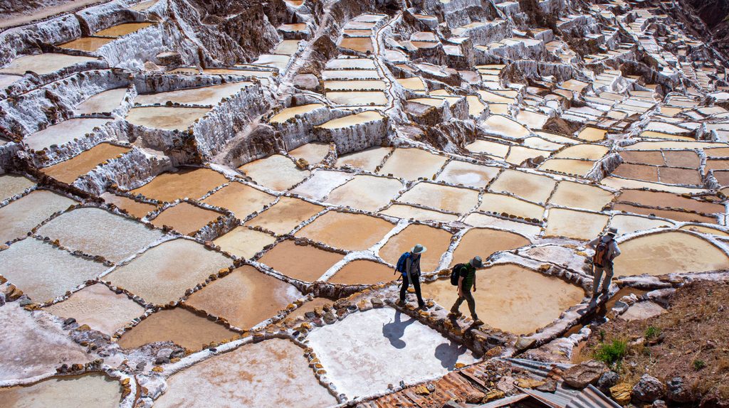 Thousands of shimmering salt terraces at the Maras Salt Mines in Peru's Sacred Valley, with visitors walking among the white and golden salt pools.